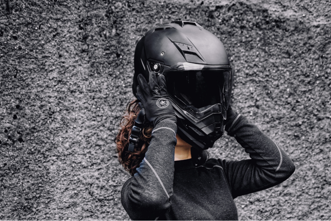 A woman putting on a helmet, getting ready for a ride on her motorcycle